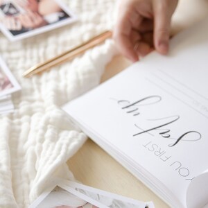 May include: A white, blank, hardcover book with the text 'You First' in black calligraphy on the front cover. The book is open to a blank page with the text 'On the first year of your life' in black text.