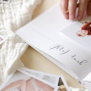 May include: A white baby memory book with a photo of a baby in a red and white outfit. The page is titled 'our first' in cursive handwriting.