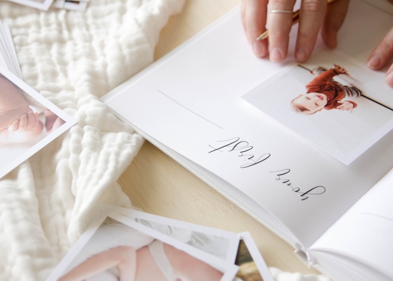 May include: A white baby memory book with a photo of a baby in a red and white outfit. The page is titled 'our first' in cursive handwriting.