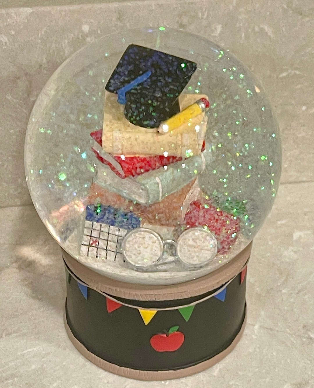 Graduation Snow Globe Featuring a Stack of Books Topped With Graduation