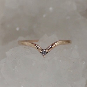 Puede incluir: Un anillo de oro en forma de V con una pequeña piedra preciosa transparente en el centro.