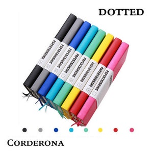 Könnte beinhalten: Ein Set aus acht Notizbüchern mit gepunktetem Papier, jedes mit einem anderen farbigen Einband. Die Einbände sind schwarz, grau, blau, türkis, grün, gelb, rot und pink. Die Notizbücher sind alle mit "PAPERTHINKING" beschriftet und haben ein kleines Gitter-Symbol auf dem Etikett. Die Notizbücher sind fächerförmig angeordnet, mit dem schwarzen Notizbuch oben und dem pinken Notizbuch unten.