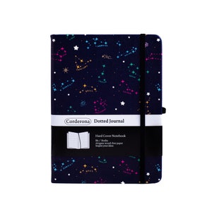 May include: A blue hard cover dotted journal with a constellation pattern. The journal has a black elastic closure and a white label that reads "Corderona Dotted Journal". The label also includes the text "Hard Cover Notebook", "B6/Boshs", "160gsm wood-free paper", and "Inspire your ideas".