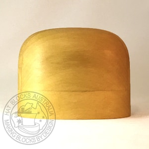May include: A golden-yellow hat block with a rounded top and a cylindrical base. The hat block is made of wood and has a smooth, polished finish. The text "HAT BLOCKS AUSTRALIA MAKING BLOCKS BY DESIGN" is printed on the side.