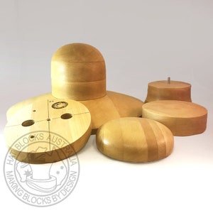 Könnte beinhalten: Eine Sammlung unfertiger Hutformen aus Holz in verschiedenen Formen und Größen. Die Formen umfassen eine Kopfform, ovale und kreisförmige Formen sowie einen zylindrischen Block mit einem Metallstift. Die Blöcke sind aus hellem Holz gefertigt.