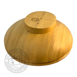 Può includere: Un blocco per cappelli in legno chiaro con una base arrotondata e una parte superiore circolare. La parte superiore presenta segni incisi ed è attaccata alla base. La base ha una forma curva. Il logo "HAT BLOCKS AUSTRALIA MAKING BLOCKS BY DESIGN" è visibile.