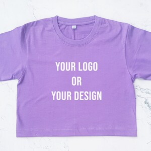 May include: A purple cropped t-shirt with the text "YOUR LOGO OR YOUR DESIGN" printed in white on the front.