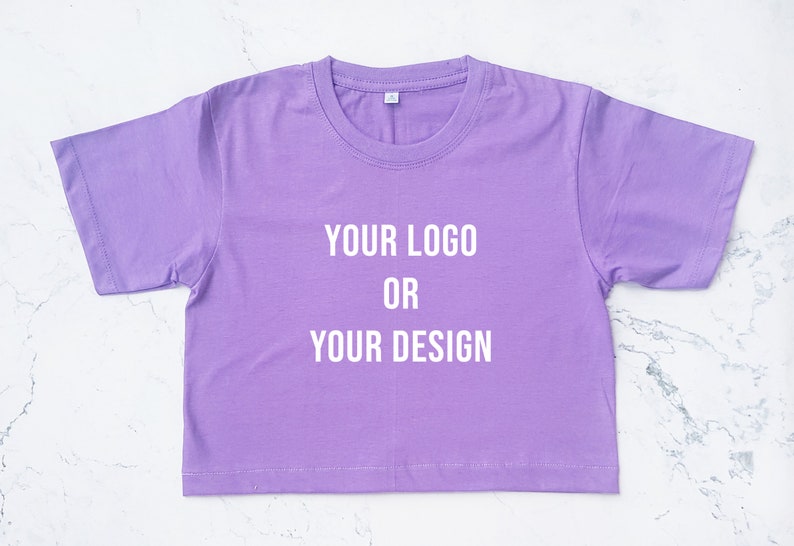 May include: A purple cropped t-shirt with the text "YOUR LOGO OR YOUR DESIGN" printed in white on the front.