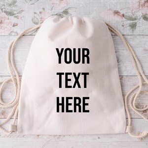 Puede incluir: Una bolsa de cordón blanco con el texto "YOUR TEXT HERE" impreso en la parte delantera. La bolsa está hecha de algodón natural y tiene un diseño sencillo.