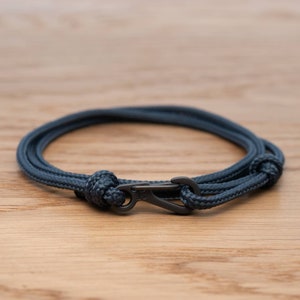 Puede incluir: Un brazalete de cuerda azul oscuro con un cierre de metal negro.