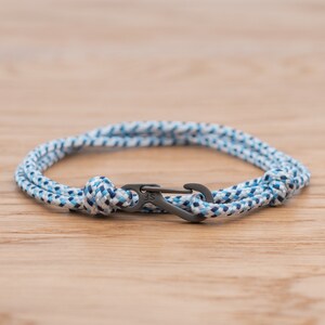 Puede incluir: Un brazalete de cuerda con estampado azul y blanco con un cierre plateado. El cierre tiene las letras "JS" grabadas.