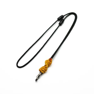 Könnte beinhalten: Ein schwarzes Lanyard mit einem geflochtenen Knoten in Gelb und Orange und einem silbernen Metallclip.
