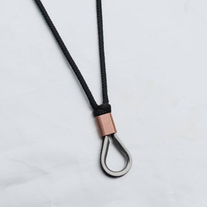 May include: A black cord necklace with a copper and silver pendant. The pendant is a simple loop shape.