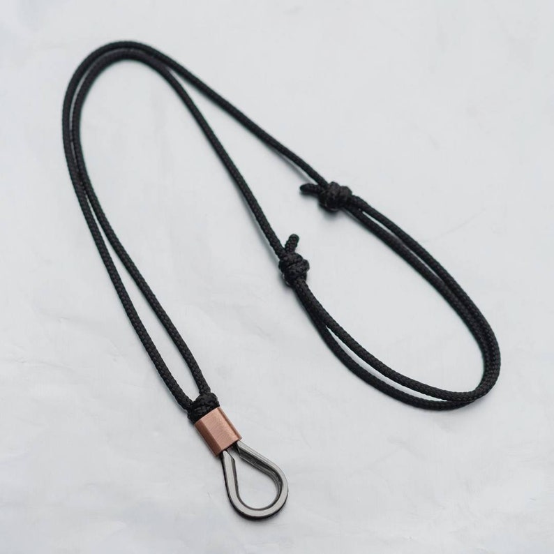 May include: A black cord necklace with a copper and silver pendant. The pendant is a small, teardrop-shaped loop.