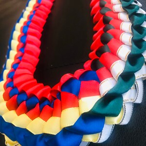 以下が含まれることがあります： サテンリボンでできた、マルチカラーのレイ。レイは、赤、青、黄、白、緑のリボンで作られています。リボンは、重ねて編まれています。