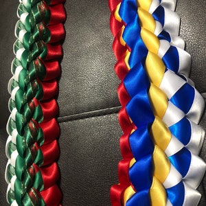 以下が含まれることがあります： 赤、緑、白のリボンと、青、黄、白のリボンでできた、手作りのレイ2つ