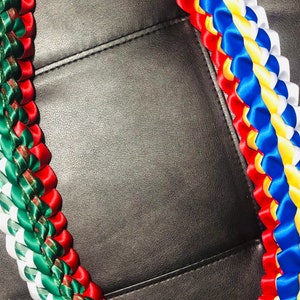 以下が含まれることがあります： 赤、白、緑、青、黄色のサテンリボンを編んだ伝統的なハワイのレイです。