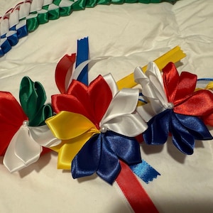 May include: A colorful braided lei with red, white, blue, yellow, and green ribbon flowers. The lei is decorated with white pearl accents.