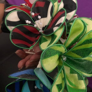 Puede incluir: Un ramo de flores de tela con patrones verdes, rojos, blancos y azules. Las flores est&aacute;n hechas de tela en capas y tienen un ribete verde. Las flores est&aacute;n decoradas con cuentas blancas.