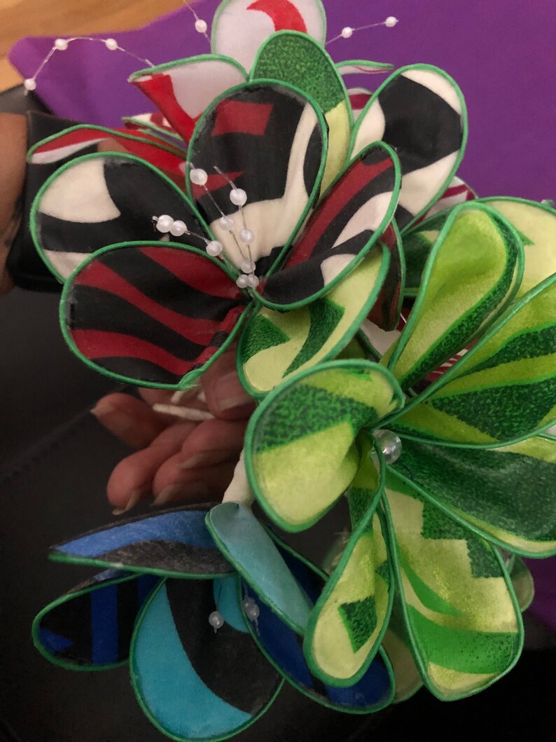 Puede incluir: Un ramo de flores de tela con patrones verdes, rojos, blancos y azules. Las flores est&aacute;n hechas de tela en capas y tienen un ribete verde. Las flores est&aacute;n decoradas con cuentas blancas.