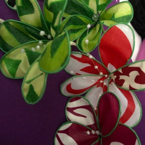Puede incluir: Primer plano de una tela morada con un dise&ntilde;o floral. Las flores est&aacute;n hechas de tela y tienen colores verde, rojo, blanco y burdeos. Las flores est&aacute;n decoradas con cuentas blancas.