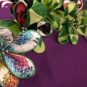 Puede incluir: Cinco flores de tela con bordes verdes y varios patrones coloridos. Las flores est&aacute;n dispuestas en semic&iacute;rculo sobre una superficie morada.