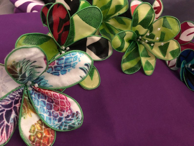 Puede incluir: Cinco flores de tela con bordes verdes y varios patrones coloridos. Las flores est&aacute;n dispuestas en semic&iacute;rculo sobre una superficie morada.