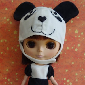 May include: A doll wearing a panda bear costume, including a white hat with black ears and facial features, a white top, and black shorts. The doll has brown eyes and red hair. The background is orange with yellow stars and the words "Trick or Treat".