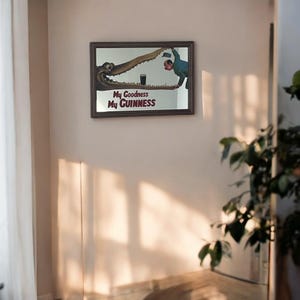 May include: A framed mirror with a vintage Guinness advertisement featuring a crocodile and a man holding a glass of beer. The text on the advertisement reads "My Goodness My GUINNESS".