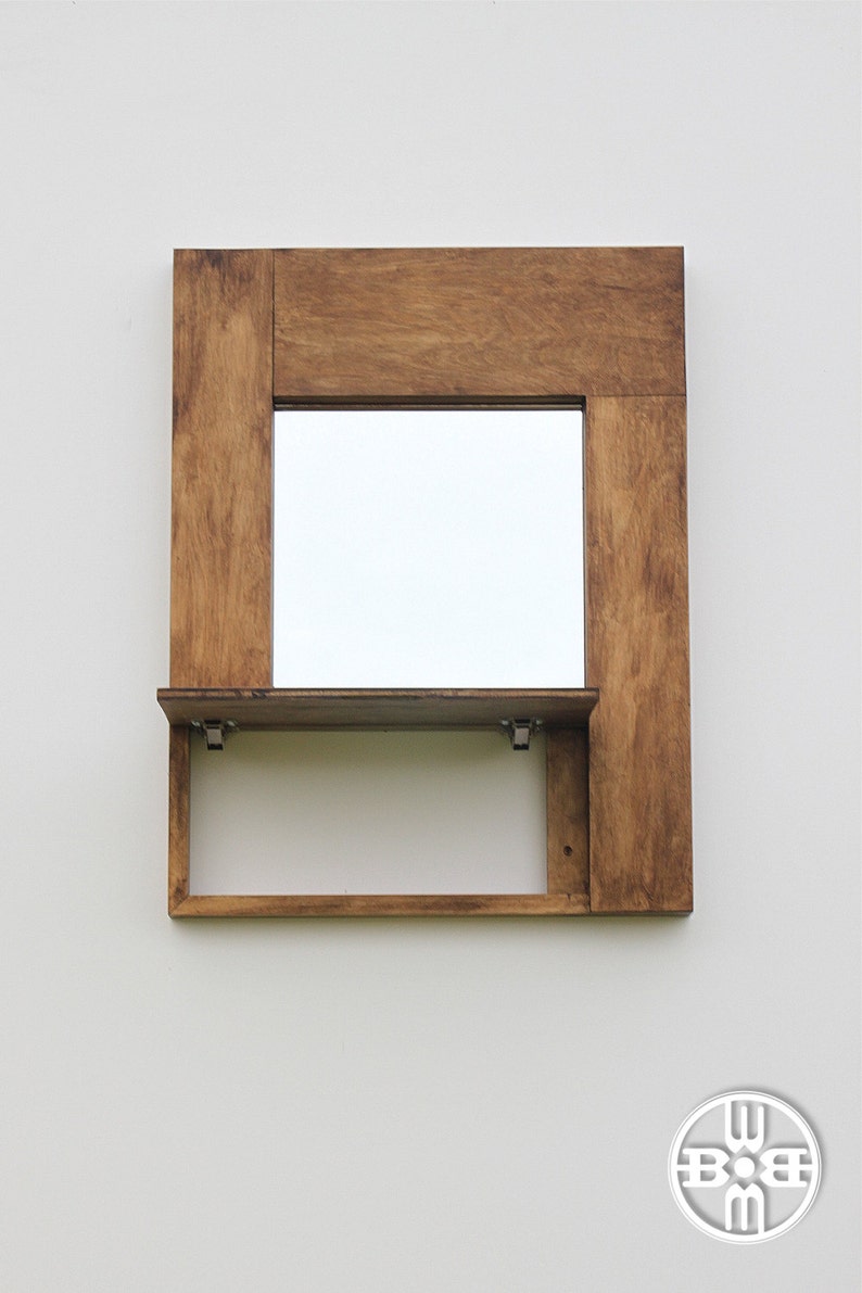 Puede incluir: Un espejo con marco de madera y un estante debajo. El espejo es rectangular y el marco es de color marr&oacute;n oscuro.