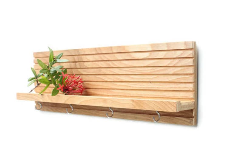 Pu&ograve; includere: Un ripiano a muro in legno con un design a doghe e un ripiano con quattro ganci. Il ripiano &egrave; in legno chiaro e ha una finitura naturale. Un fiore rosso &egrave; sul ripiano.