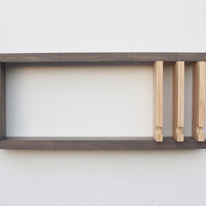 May include: A dark gray wooden shelf with three light wood dividers. The shelf is mounted on a white wall.