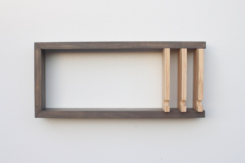 May include: A dark gray wooden shelf with three light wood dividers. The shelf is mounted on a white wall.
