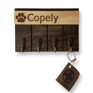 May include: A wooden key holder with four hooks and a paw print design. The holder has a personalized nameplate that reads "Copely".