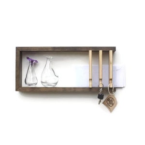 May include: A wooden key holder with four hooks and a small shelf. The shelf has two clear glass vases with purple flowers. The key holder is mounted on a white wall.