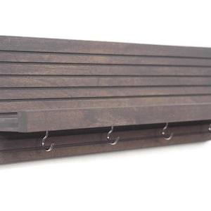 May include: A dark brown wooden wall mounted shelf with a slatted back and a small shelf. The shelf has four metal hooks underneath.