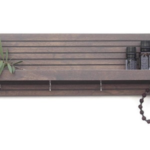 May include: A gray wooden shelf with a slatted back and a small shelf on the front. There are five small bottles on the top shelf and a beaded necklace hanging from a hook on the bottom shelf.