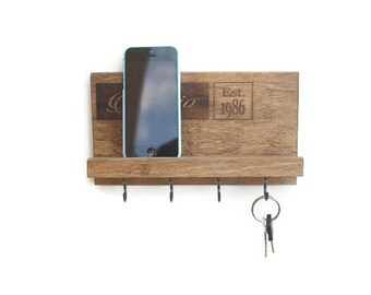 May include: A wooden key holder with a shelf for a phone and hooks for keys. The holder is engraved with the text "Est. 1986".