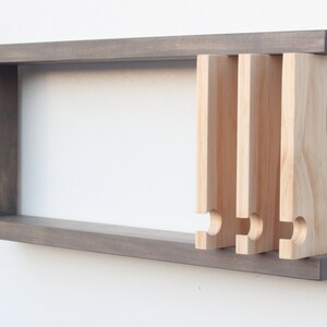 May include: A gray wooden wall shelf with a rectangular opening and five wooden pegs protruding from the side. The pegs have a rounded, curved shape at the bottom.