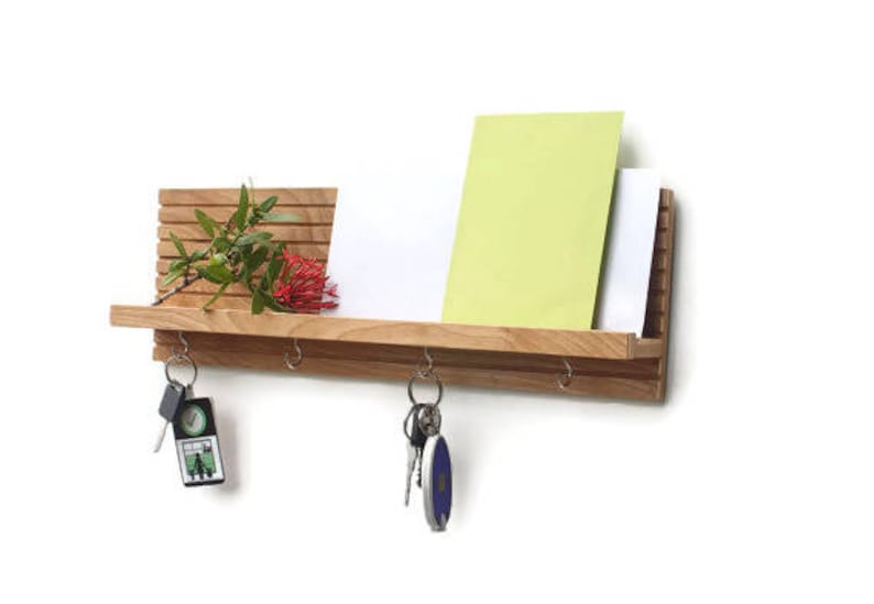 Pu&ograve; includere: Un ripiano a muro in legno con un portachiavi e una piccola pianta. Il ripiano &egrave; in legno chiaro ed &egrave; progettato per contenere chiavi, posta e altri piccoli oggetti.
