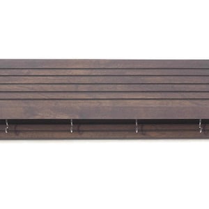 May include: A dark brown wooden wall shelf with a slatted back and four metal hooks. The shelf has a small ledge on the front.