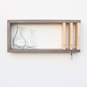 May include: A gray wooden wall shelf with two clear glass vases and a key rack with keys hanging from it.