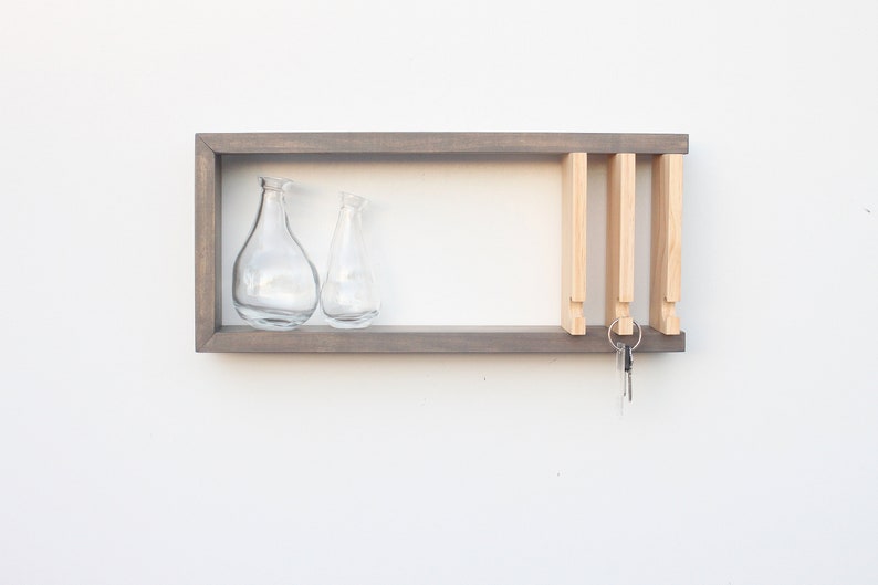 May include: A gray wooden wall shelf with two clear glass vases and a key rack with keys hanging from it.