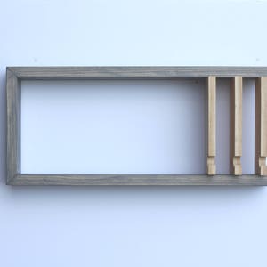 Puede incluir: Una estanter&iacute;a de madera gris con cuatro divisores verticales de madera. La estanter&iacute;a est&aacute; montada en una pared blanca.