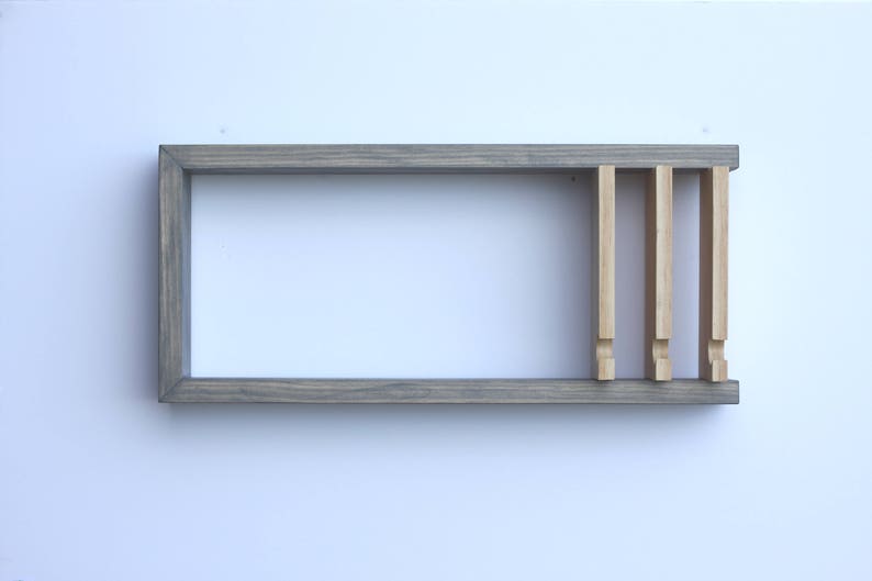 Puede incluir: Una estanter&iacute;a de madera gris con cuatro divisores verticales de madera. La estanter&iacute;a est&aacute; montada en una pared blanca.