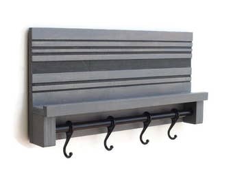 Puede incluir: Estante de pared de madera gris con una barra de metal negro y cuatro ganchos. El estante tiene un diseño a rayas gris y negro.
