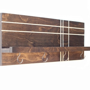 May include: A dark brown wooden wall shelf with a white geometric design. The shelf has a small ledge and four metal hooks.