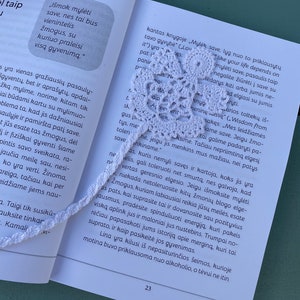 Könnte beinhalten: Nahaufnahme eines weißen Häkel-Lesezeichens mit einem zarten Blumenmuster. Das Lesezeichen liegt auf einer Buchseite mit Text über Selbstliebe und die Wichtigkeit, auf sich selbst aufzupassen.