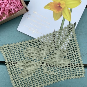 Puede incluir: Un encaje de ganchillo verde con forma cuadrada y un patrón delicado. El encaje está sobre una superficie de madera azul. El texto de la tarjeta dice "Wishing you all the lovely things that make everything so special".