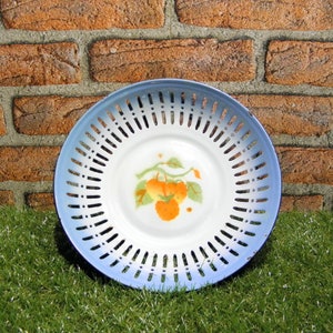 May include: A white enamel fruit bowl with a blue rim and a floral design of orange fruit. The bowl has a decorative openwork pattern.